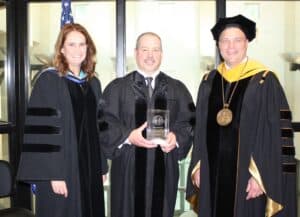 Provost Cathy Monteroso, left, and President Tim Borchers, far right, present a commemorative gift to Mickey Marotti who served as the commencement speaker.